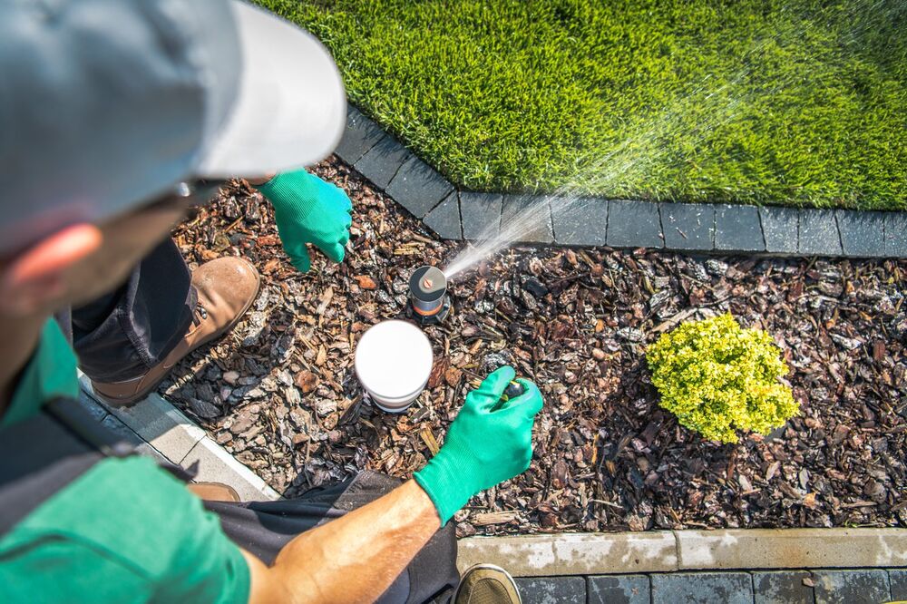Technician adjusting an irrigation spray head beside a landscape bed