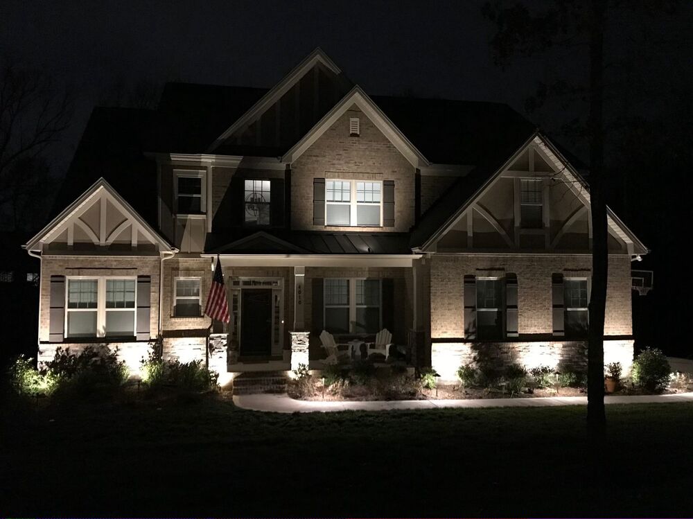 Landscape lighting washing the stone facade and front beds of a home at night