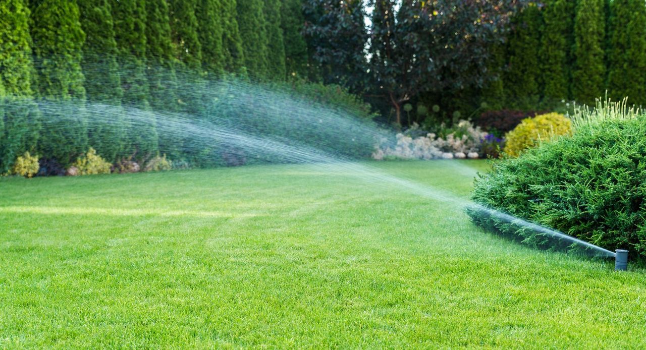 Irrigation system spraying arcs of water across a healthy green lawn and landscape beds